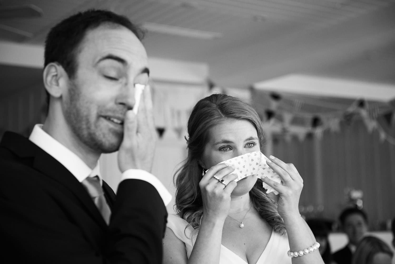 bride and groom both crying during the ceremony with tissues drying their eyes in black and white