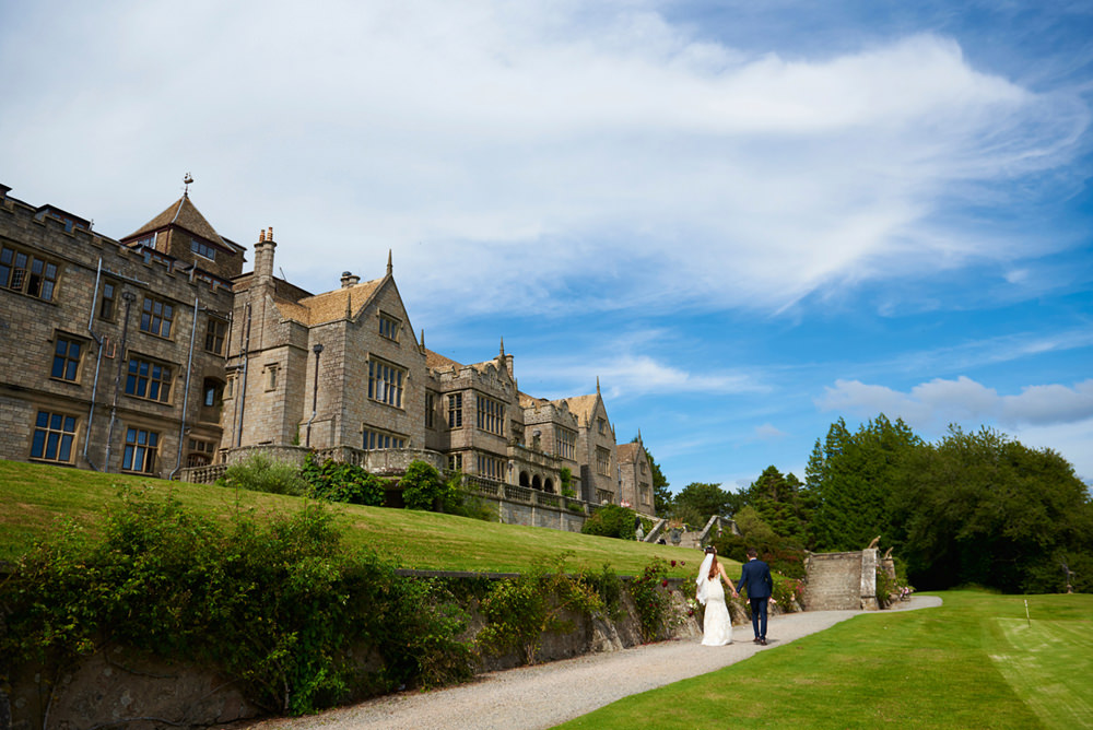 bride and groom walking away towards Bovey Castle with blue sky