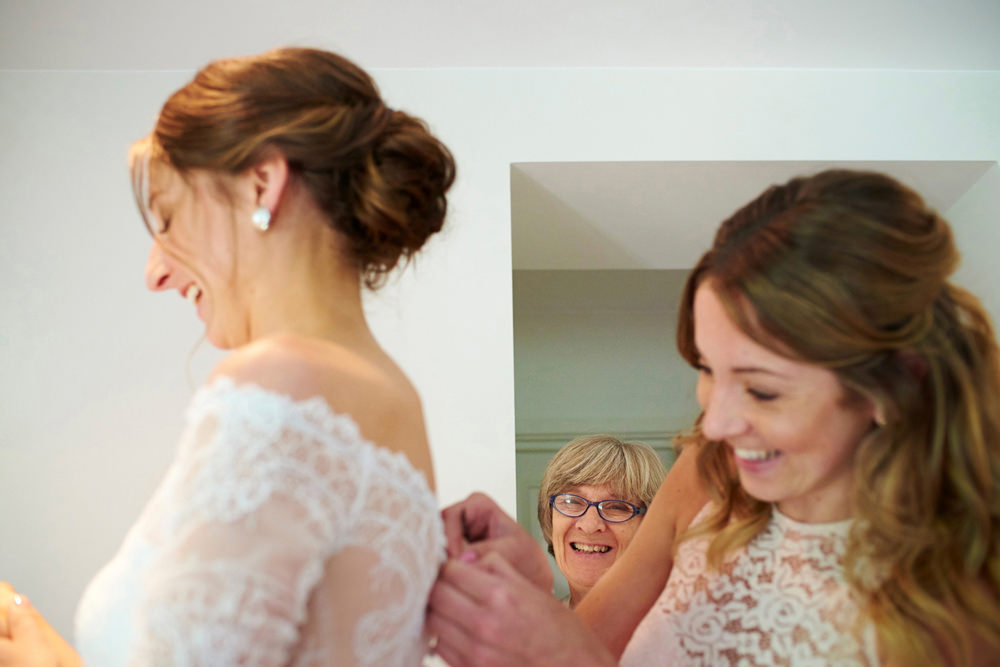 mum and sister helping bride into dress