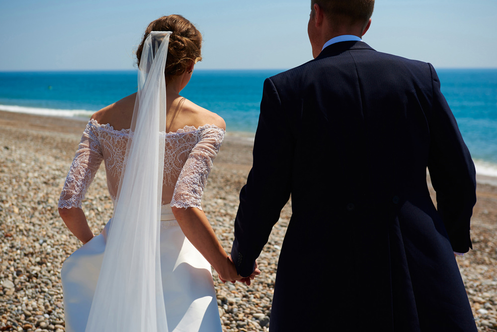 bride and groom walking towards the sea with veil