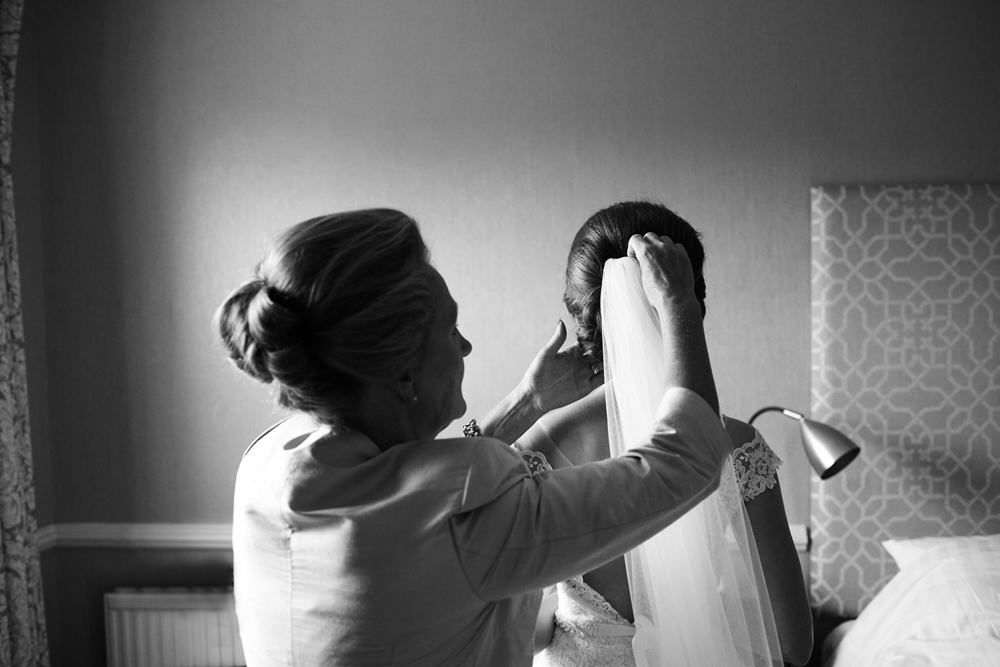 black and white of mother helping put veil on bride