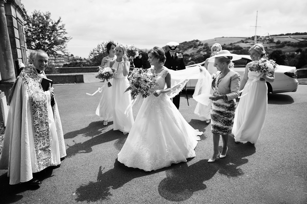 bride , bridesmaids, mum and dad in black and white walking to entrance of college
