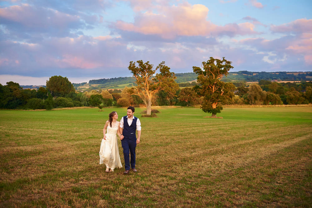 bride and groom walking in field whilst sunsets
