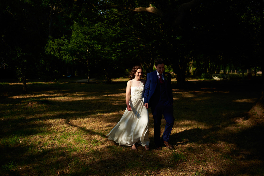 bride and groom walking through the trees in dappled light