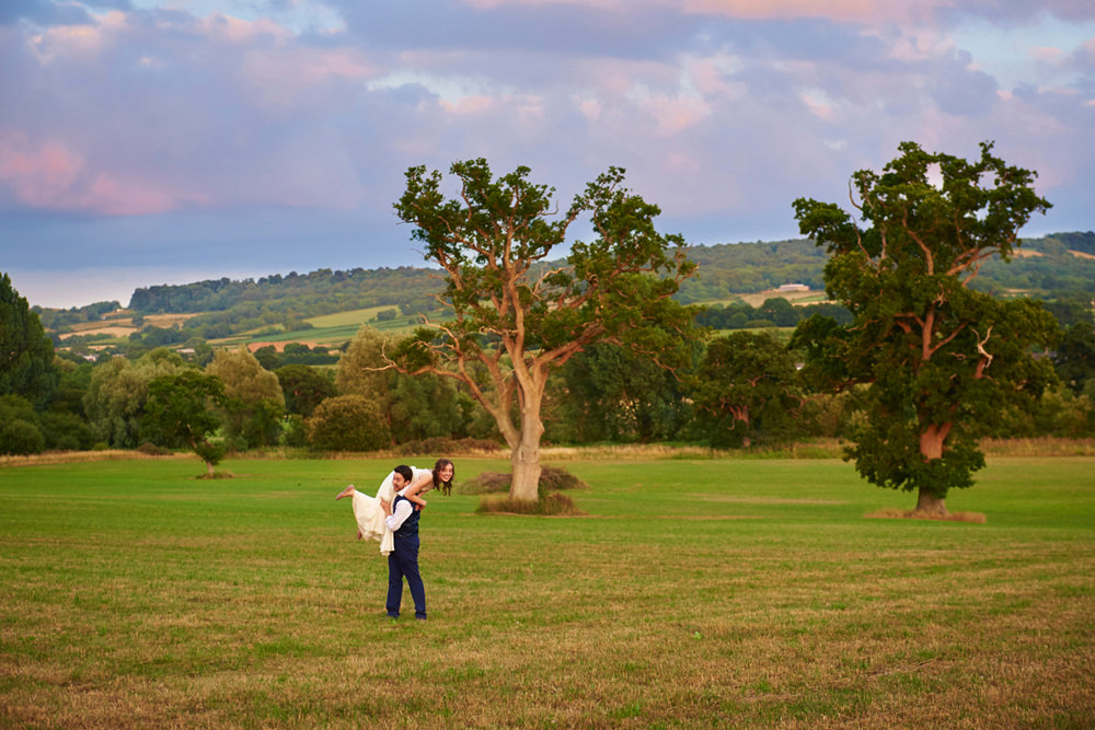 groom lifting bride over his shoulder in field