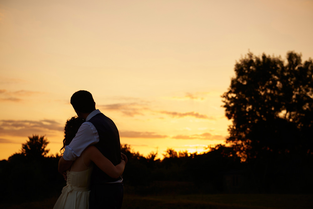 sunset shot with silhouette and groom and bride hugging