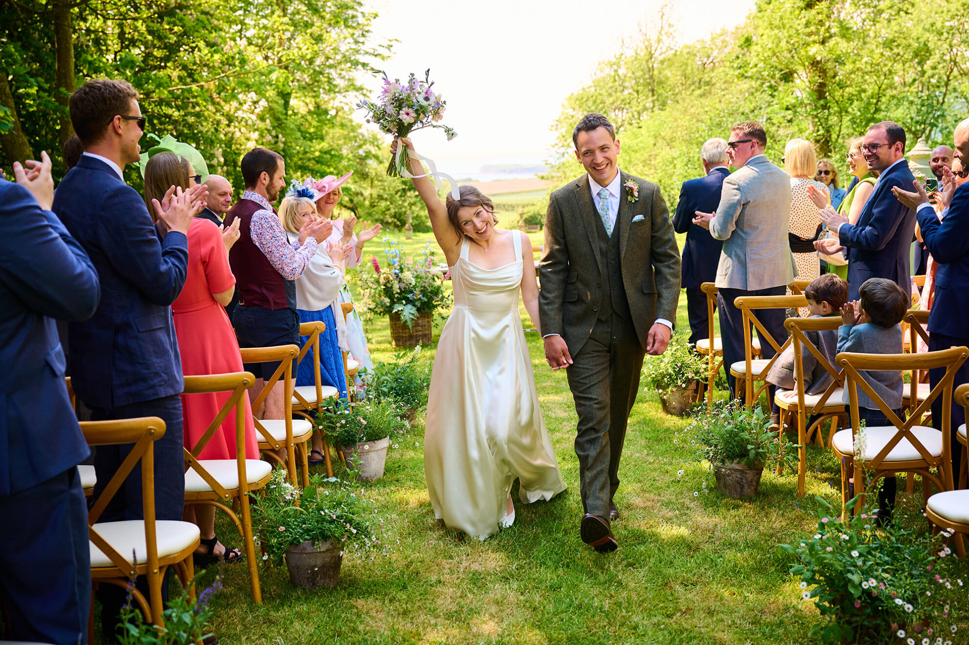 bride and groom just married at wedding and celebrating walking back up the aisle at outside ceremony at Smedmore House in Dorset with the sea in the distance